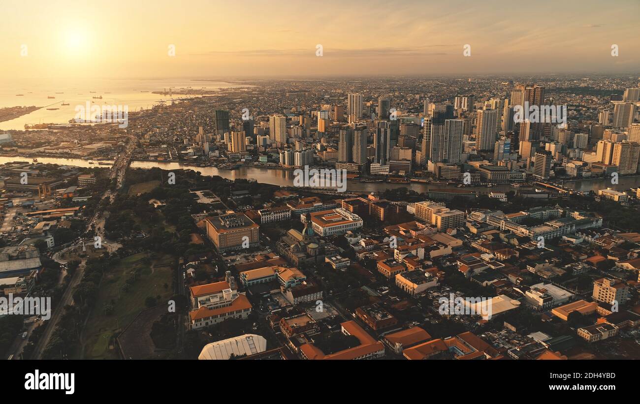 Sunrise over cityscape with green park at river shore aerial. Modern skyscrapers at business center. Traffic roadway at streets of Manila capital city, Philippines, Asia. Cinematic sun rise Stock Photo
