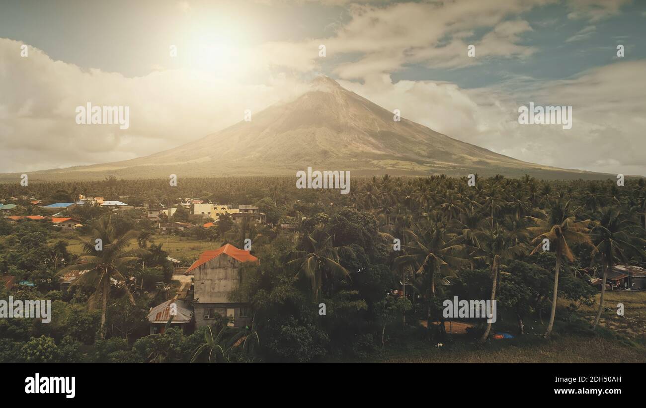 Sun cityscape of rural town at green volcano valley aerial. Contryside city streets at hillside greenery dale of Mayon mount, Philippines. Houses, cottages at tropic palm trees, plants. Road with cars Stock Photo