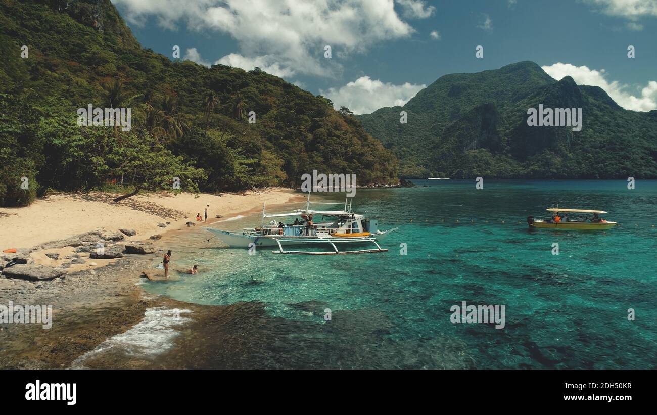 Passenger boat at ocean beach aerial view. People resting, swiming on sand at sea bay water. Amazing landscape of Philippines tropical nature with jungle forest and mountain. Cinematic paradise resort Stock Photo