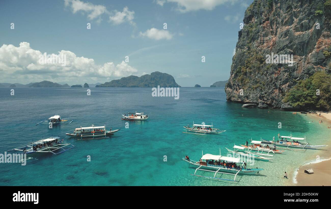 Tropic seascape at sand beach with resting tourists. Majestic landscape of harbor at El Nido island, Philippines, Asia. Closeup passenger boat at ocean bay with green cliff shore at aerial view Stock Photo