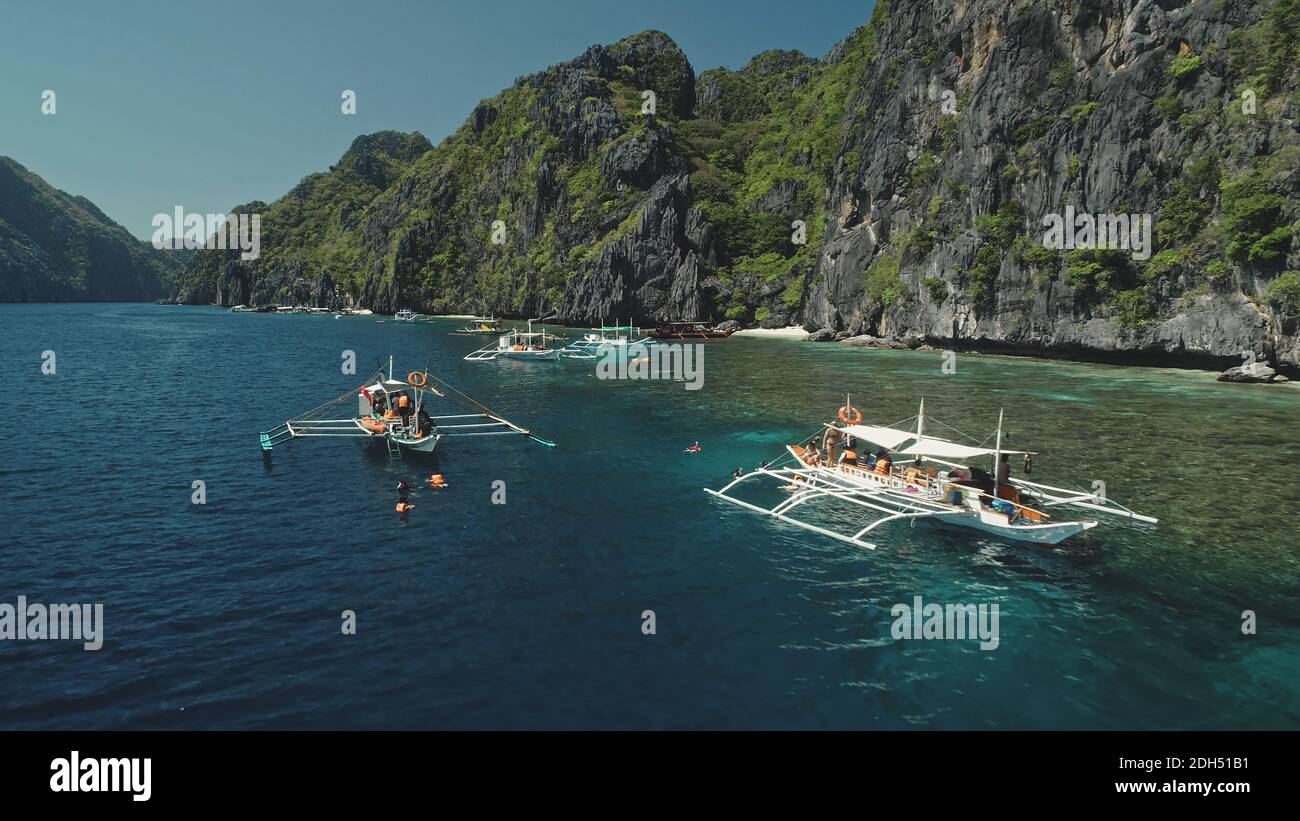 Serene tropical nature scape at mountain island of Palawan, Philippines, Visayas Archipelago. Closeup passengers boats at ocean coast with cliff shore at summer tour. Cinematic close up drone shot Stock Photo