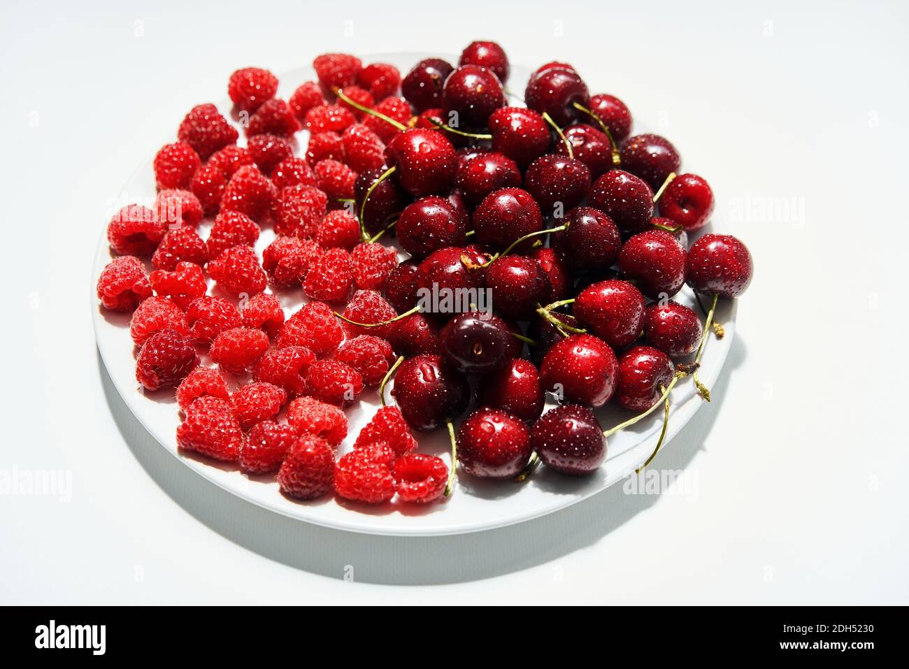 Mix of cherries and raspberries on plate isolated on white background ...