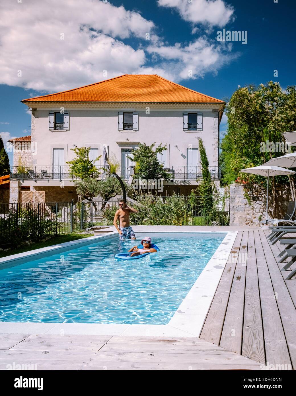 French vacation home with wooden deck and swimming pool in the Ardeche France. Couple relaxing by the pool with wooden deck duri Stock Photo