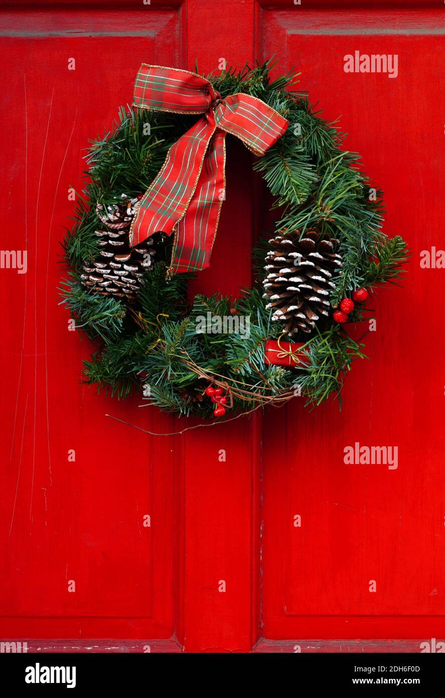Christmas holiday pine wreath with pinecones and red bow on a red door ...