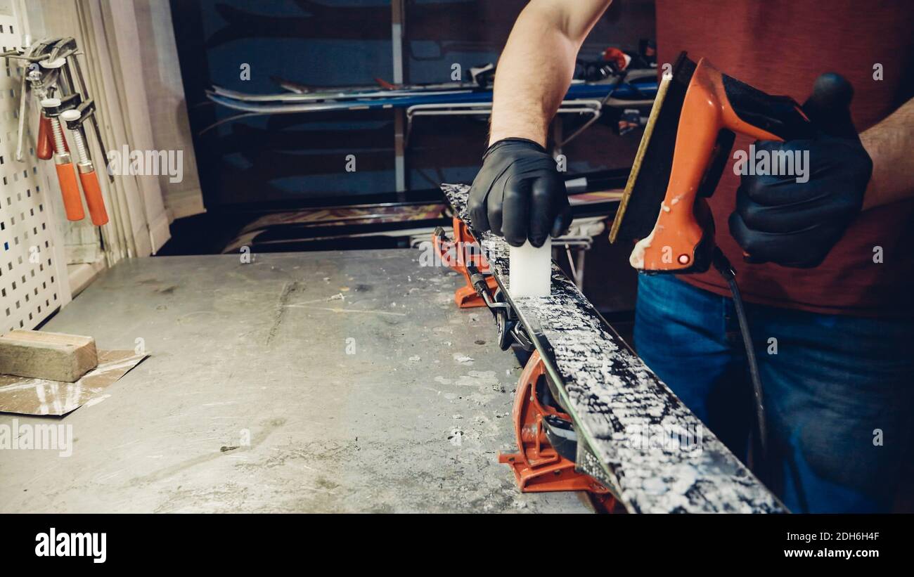 Applying hot wax to ski base with iron. Applying Ski Wax To Ski Base. Ski base tuning. Ski wax iron and wax bars. Ski service an Stock Photo