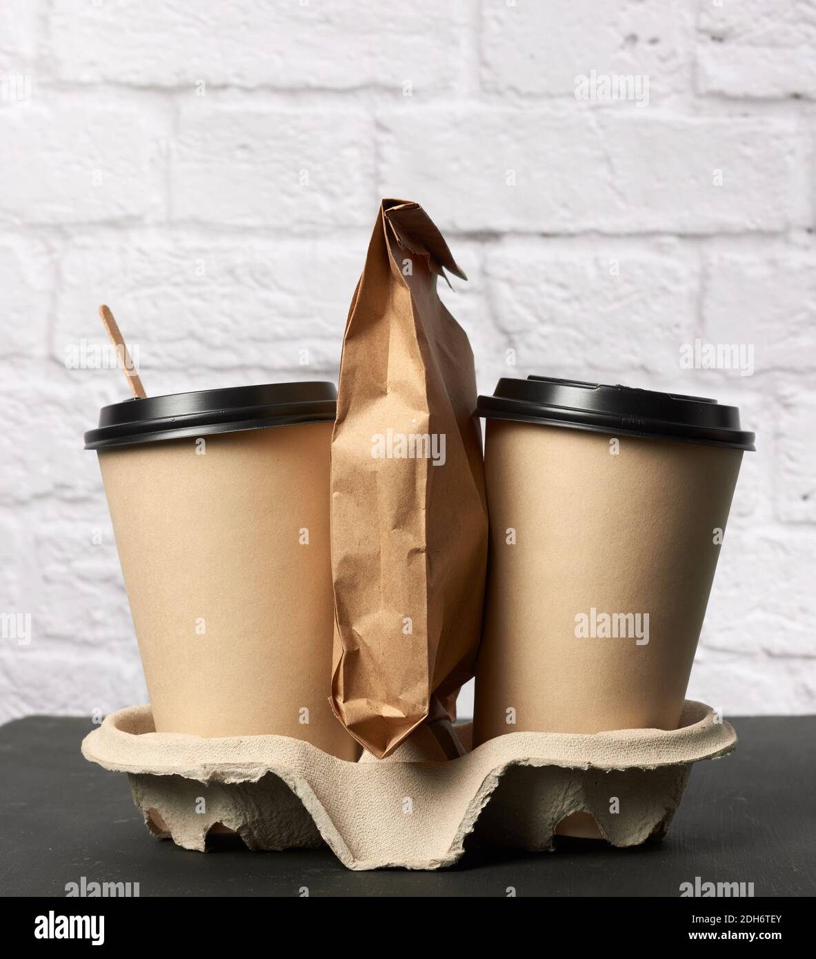 Two brown paper disposable cups with a plastic lid stand in the tray ...