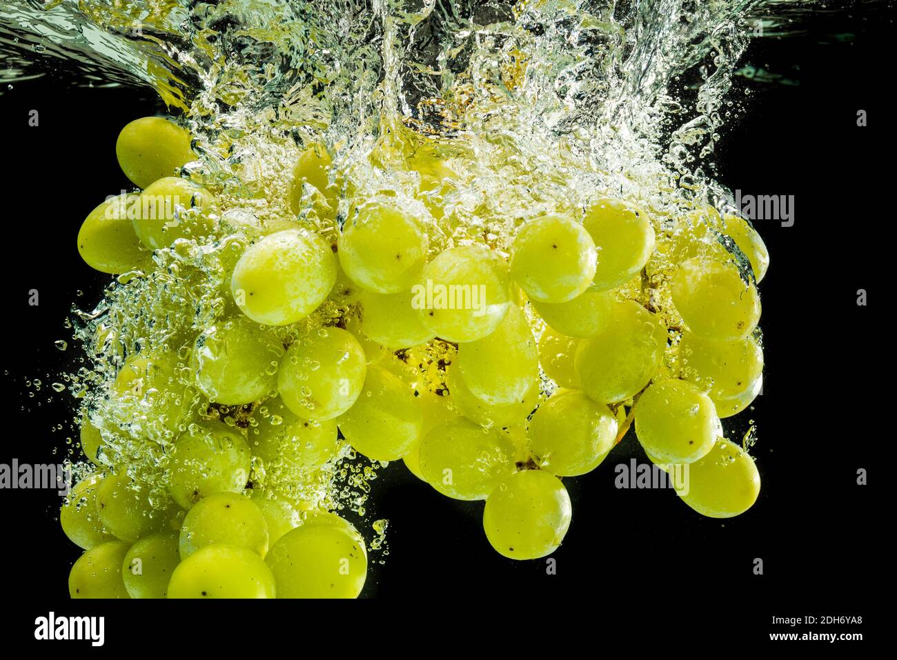 Bunch of white grapes splashing into clear water isolated against black background. Food splash photography Stock Photo