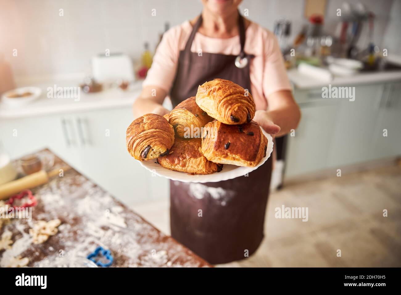 Hospitable woman holding plate with pastries in extended hands Stock