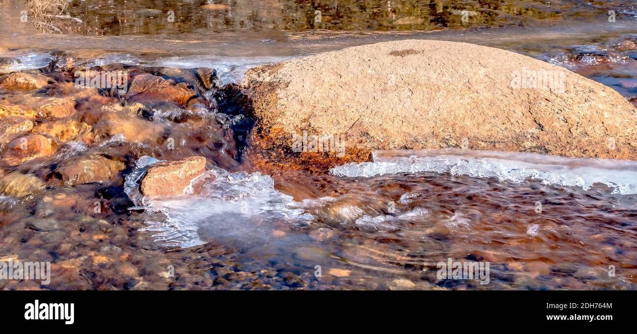 Frozen spring  and ice thawing around big rock Stock Photo