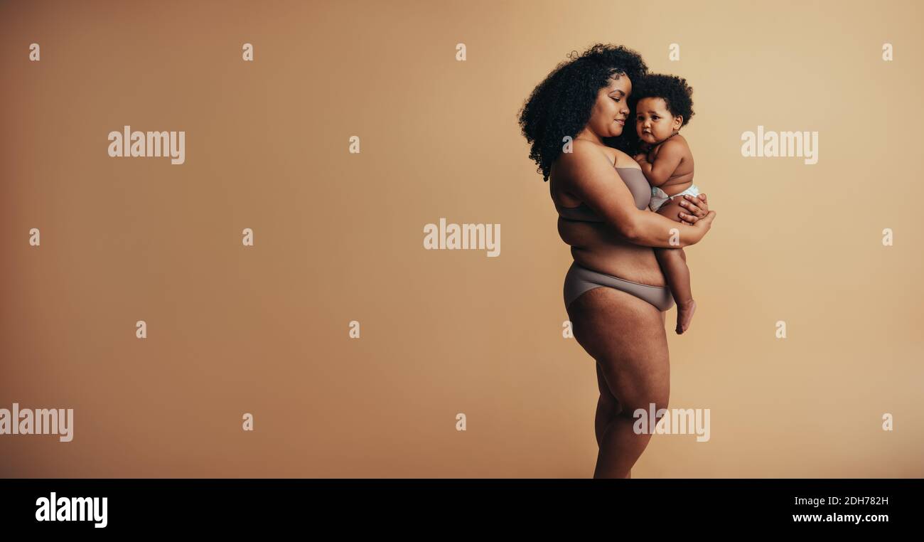 African american woman carrying her child in her arms in studio. Caring mother with her baby. Stock Photo