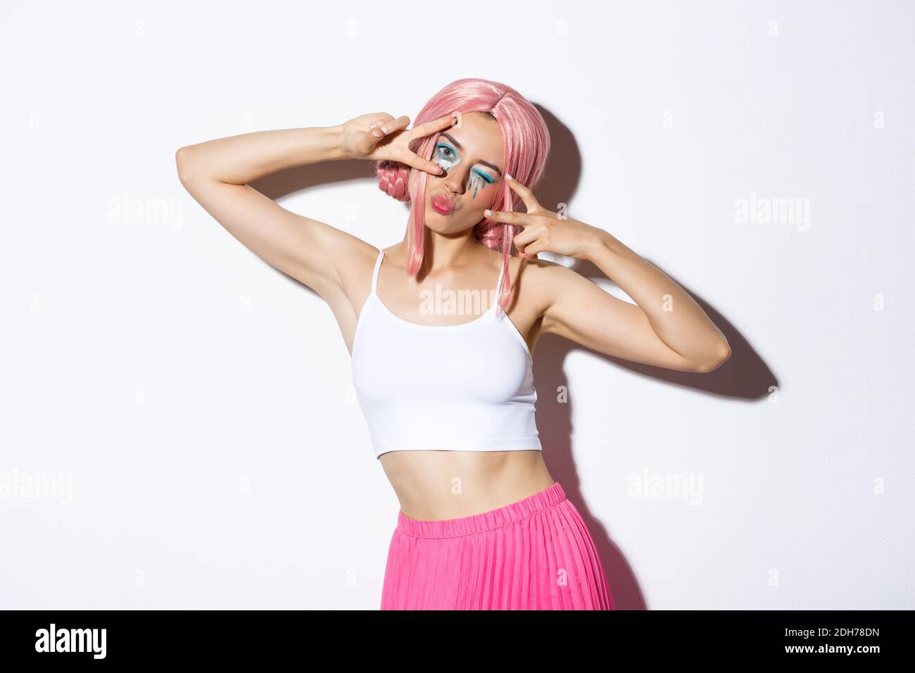 Carefree stylish girl with pink wig and bright makeup, having fun on party, celebrating and dancing, showing peace signs, standi Stock Photo