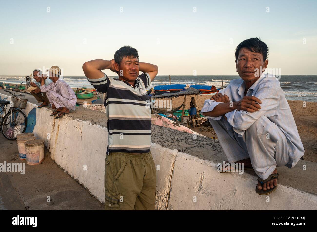 Men chatting and hanging out on the seawall, Phuoc Hai, Vietnam Stock Photo