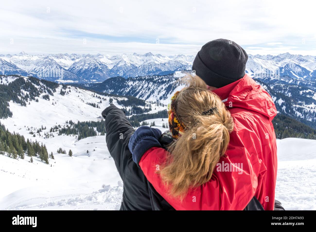 Senior couple is hiking in alpine snow winter mountains enjoying panorama view and pointing with finger to mountain peaks. Allgau, Bavaria, Germany. Stock Photo