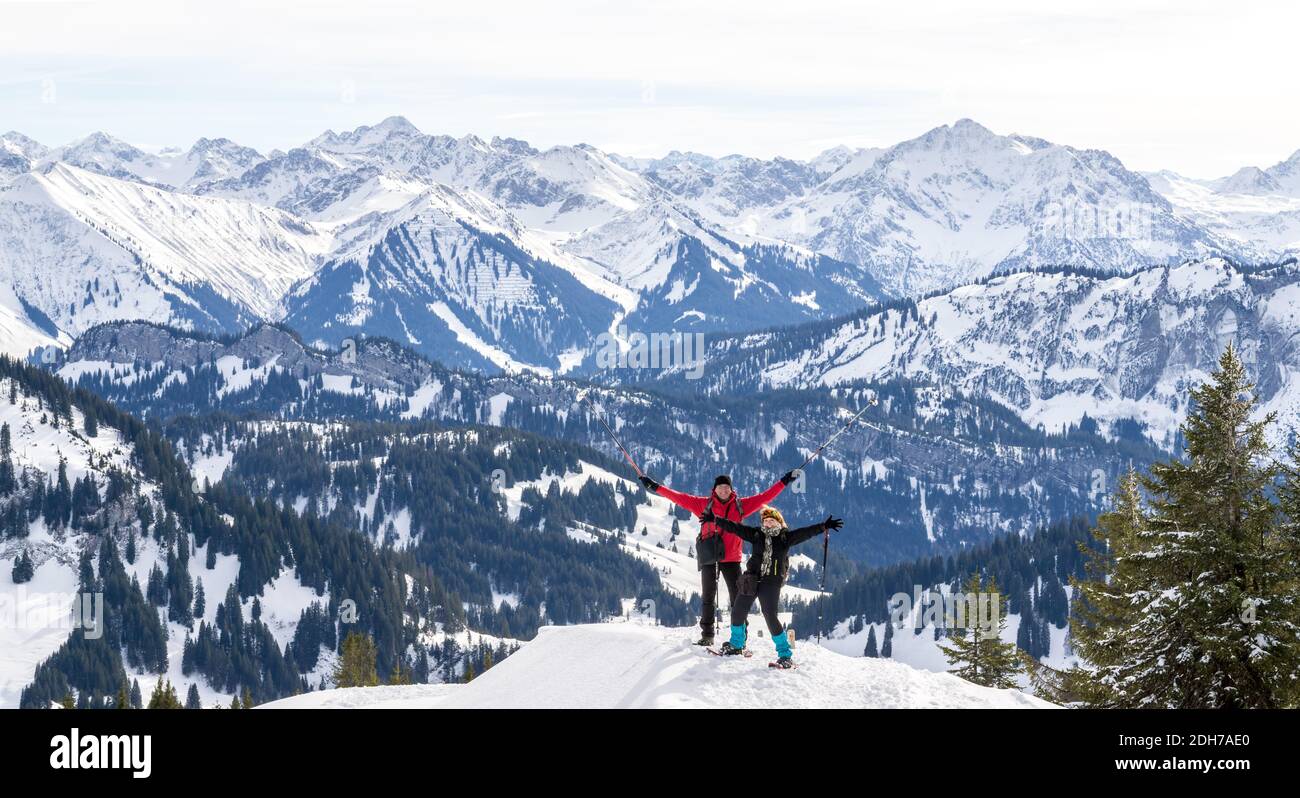 Senior couple is snowshoe hiking in alpine snow winter mountains panorama. Happy successful People with outstrechted arms. Allgau, Bavaria, Germany. Stock Photo