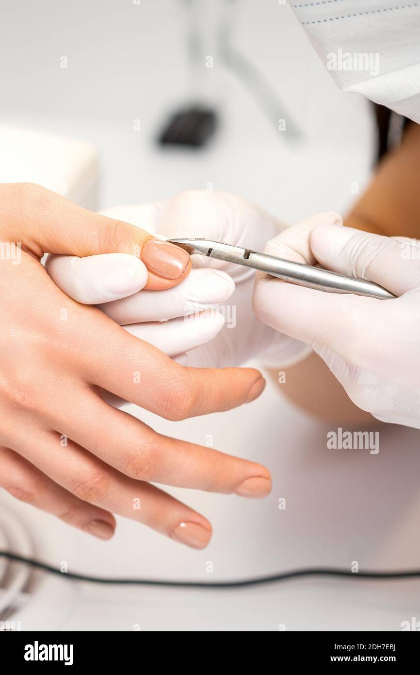 Manicure master is removing cuticles with a nail clipper in a nail