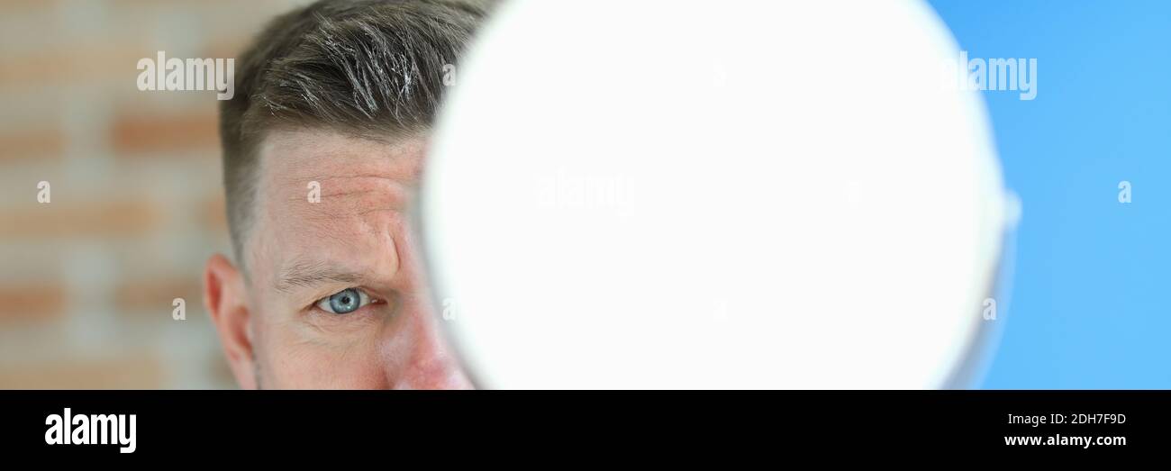 Young man with remnants of hair paste on head stands with mirror in hands portrait Stock Photo