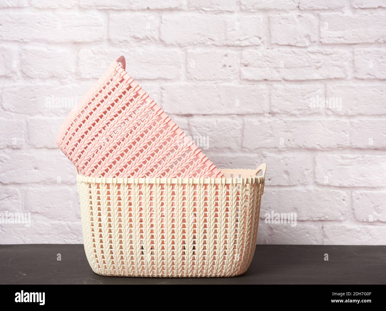 Empty white and pink wicker laundry baskets on white brick wall background Stock Photo