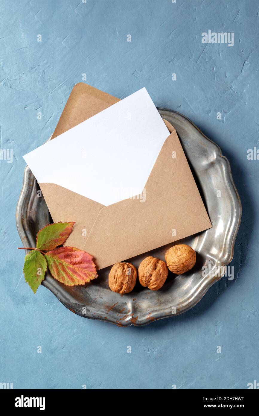 A mockup of an A5 greeting card or invitation in a brown kraft envelope, shot from the top on a tray with autumn leaves and nuts Stock Photo