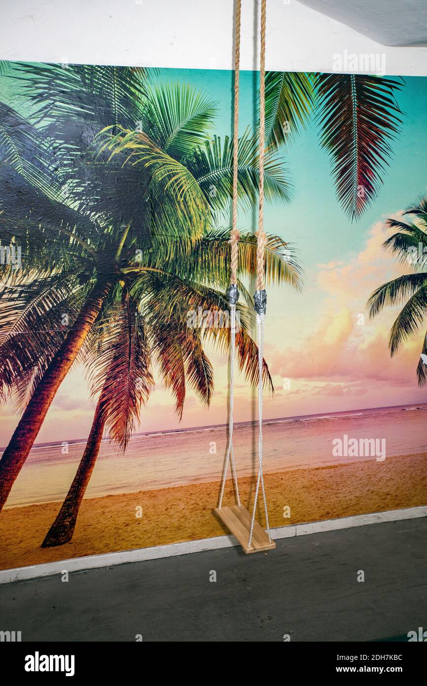 Palm tree wall paper with hanging swing by the ocean, dreams and memories of vacation and relaxation Stock Photo