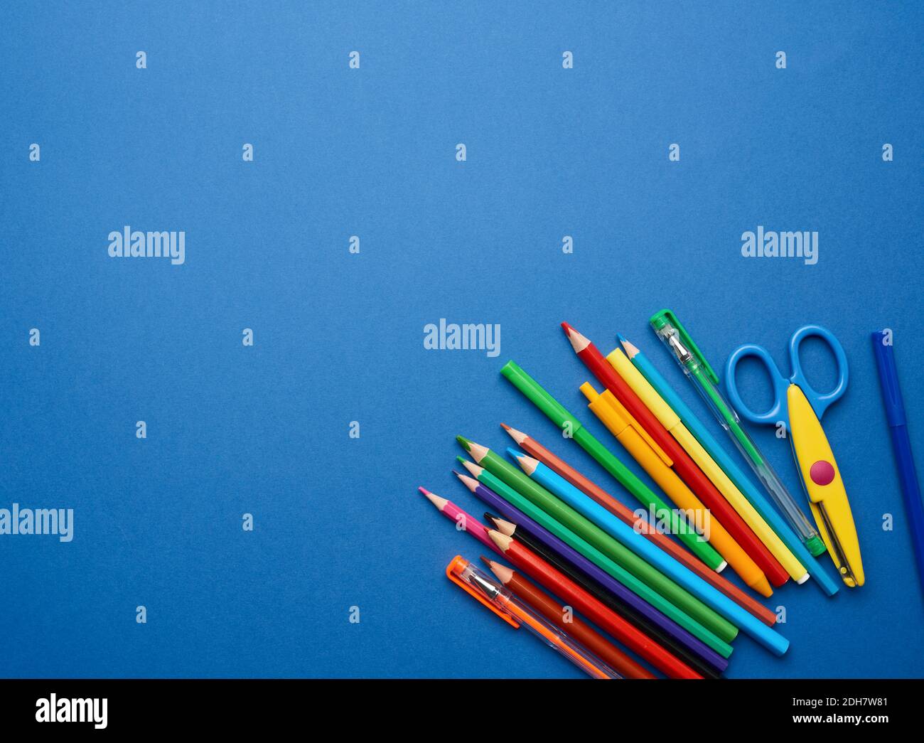 Plastic scissors and multicolored wooden pencils on a blue background Stock Photo