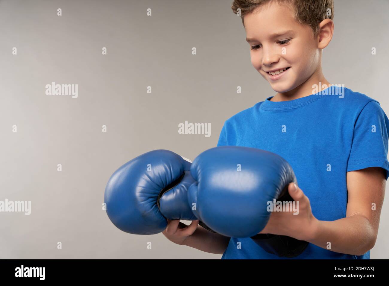 Adorable male kid looking at boxing gloves and smiling while standing