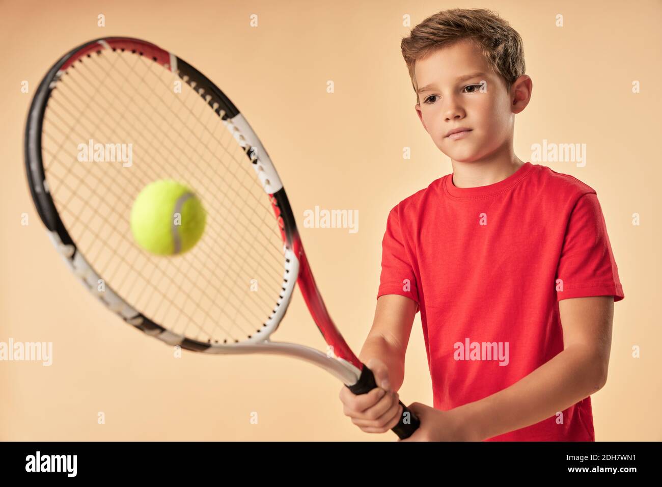 Cute male child tennis player hitting the ball with racket while