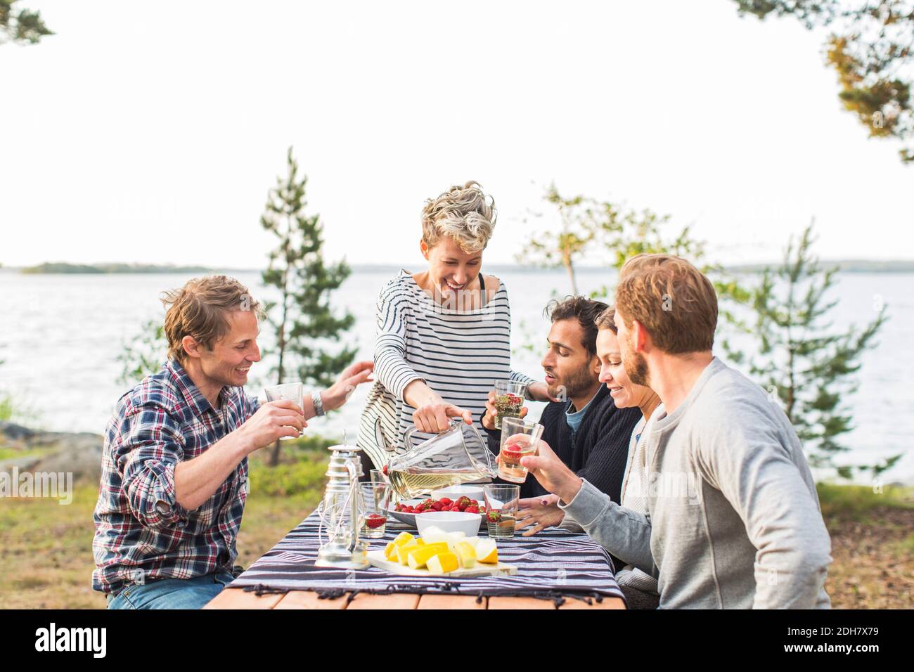 Happy woman serving beer to friends during lunch at lakeshore Stock Photo