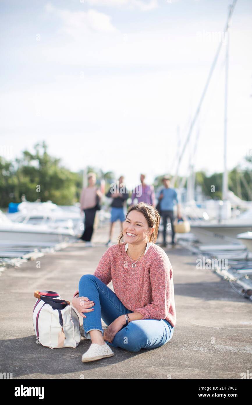 Happy woman sitting on pier with friends standing in background Stock Photo