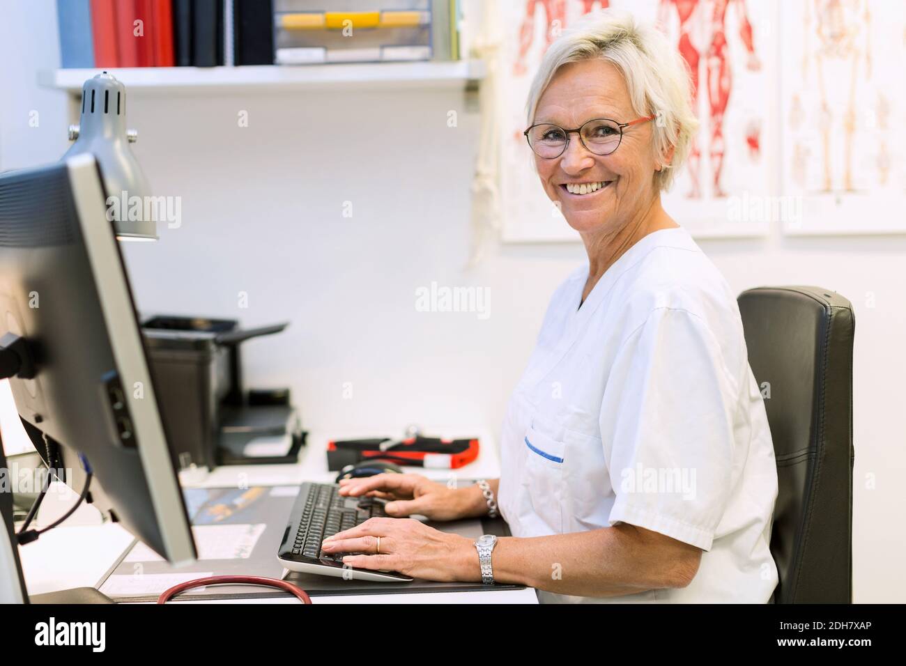 Portrait of happy senior orthopedic surgeon using computer at desk in