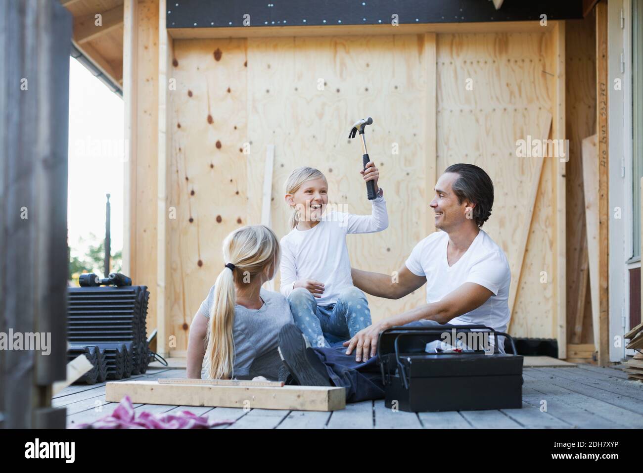 Happy parents with daughter holding hammer while sitting outside house Stock Photo