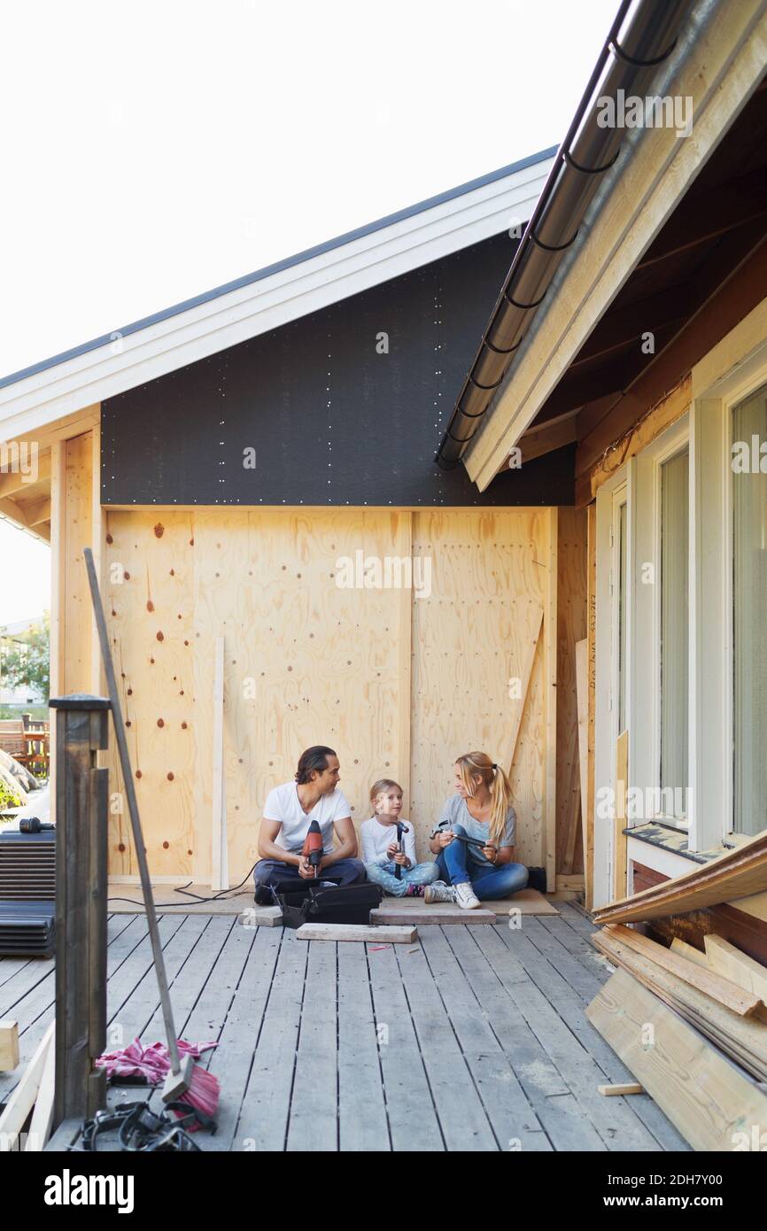 Happy family with construction tools sitting outside house Stock Photo