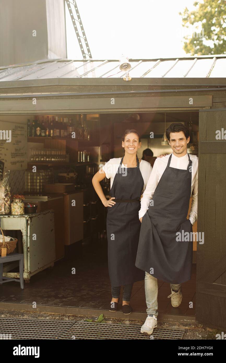 Full length portrait of smiling owners standing outside restaurant Stock Photo