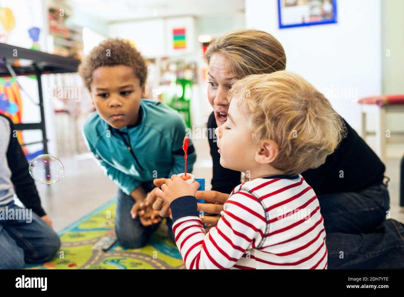 Teacher and children playing with bubbles in kindergarten Stock Photo