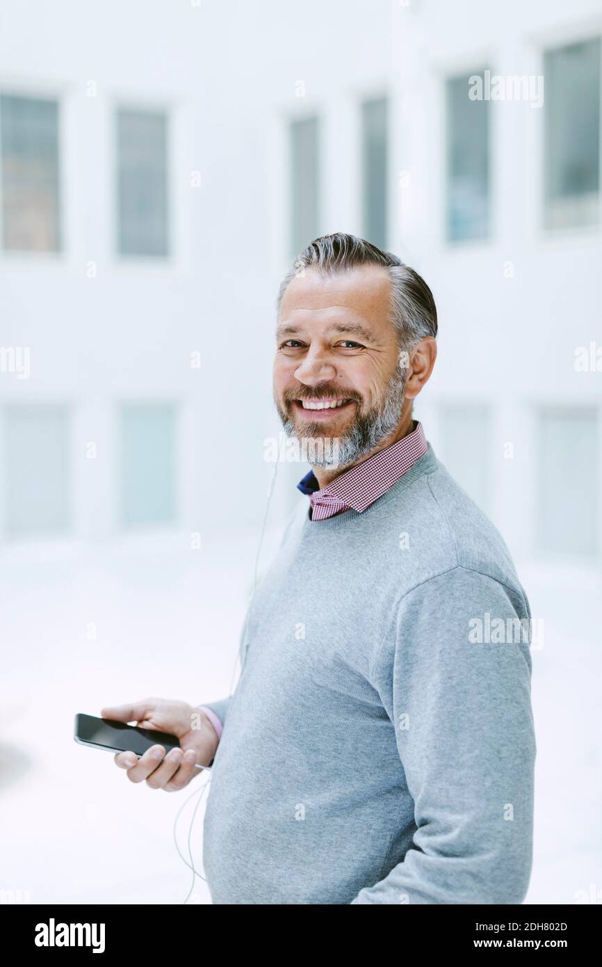 Portrait of happy businessman listening music through smart phone in office Stock Photo
