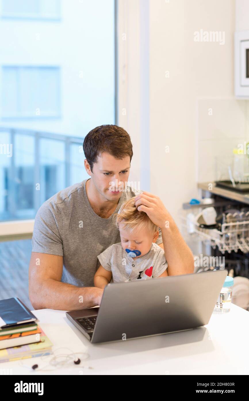 Baby boy sitting with father using laptop at table in house Stock Photo ...