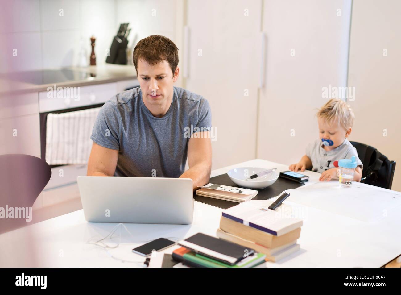 Father using laptop while baby boy sitting at dining table Stock Photo