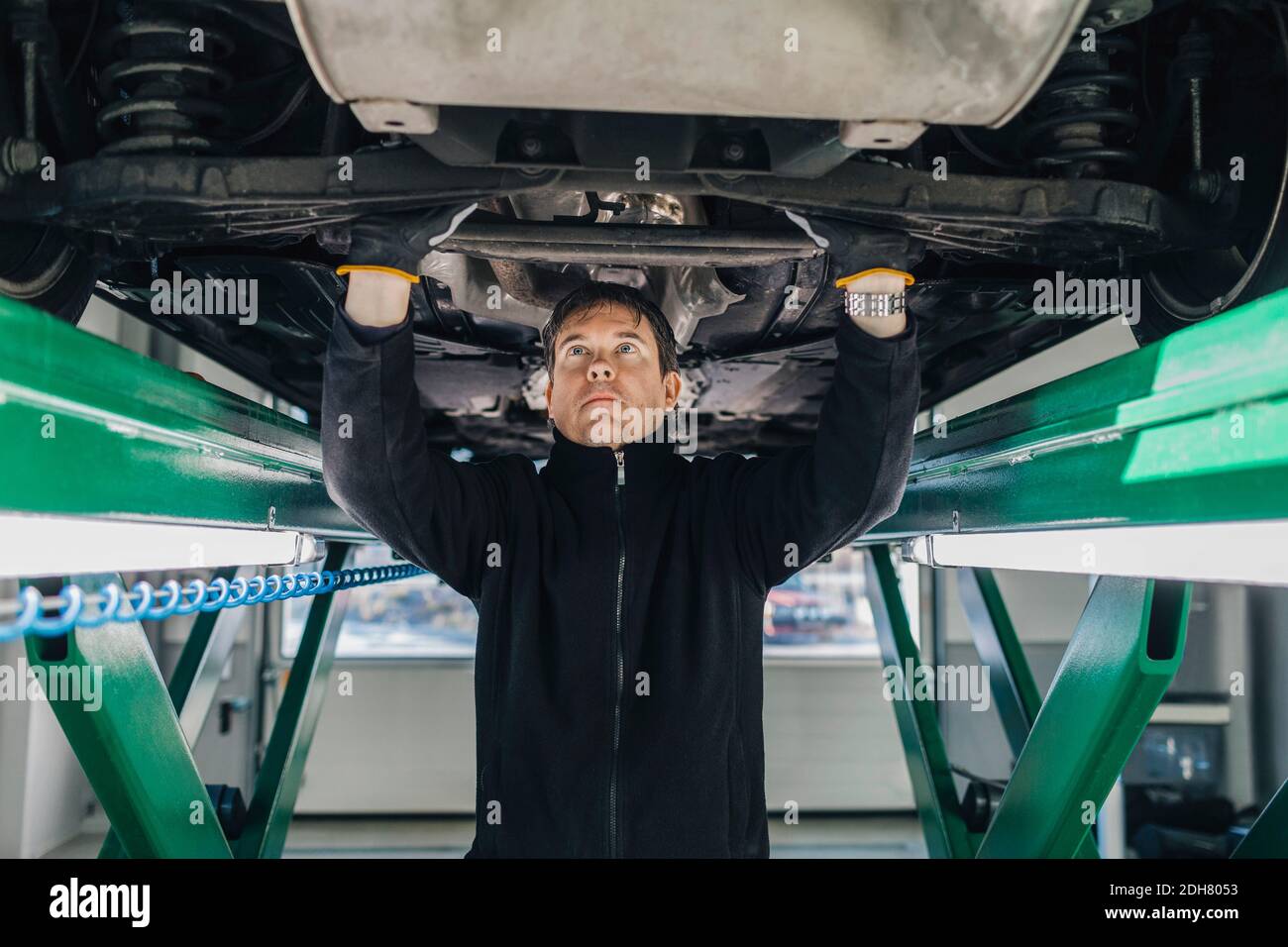 Male mechanic examining car on hydraulic lift in auto repair shop Stock ...