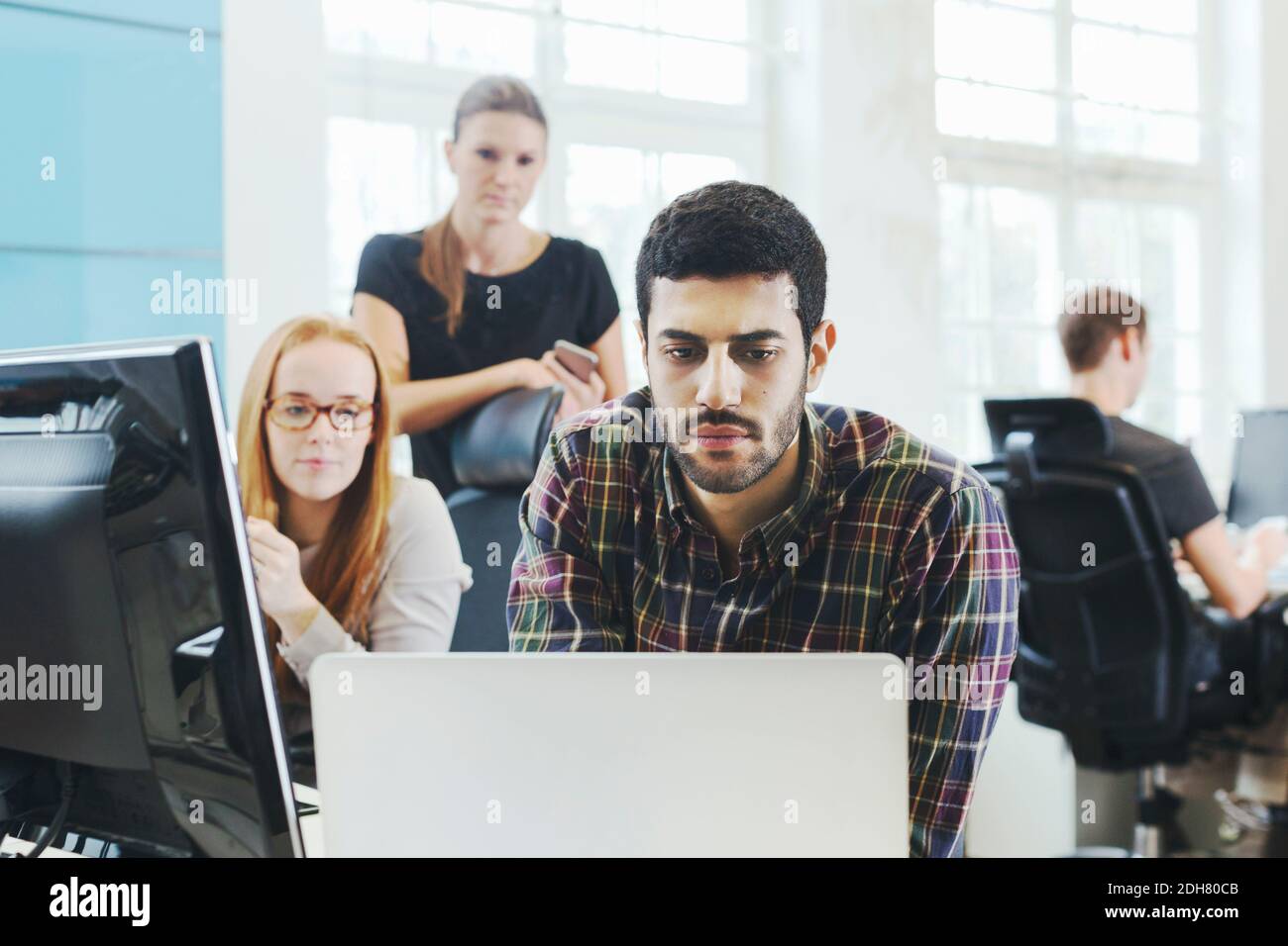 Businesswomen looking at male colleague using laptop at desk in creative office Stock Photo