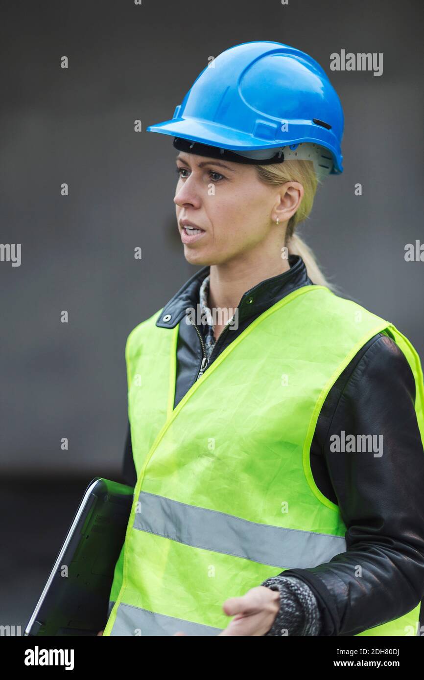 Female manual worker talking while holding laptop at factory Stock Photo