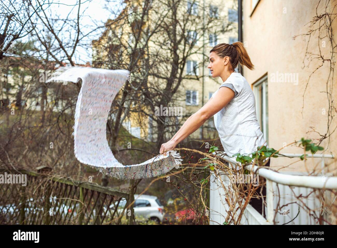 Side view of woman dusting carpet while standing in balcony Stock Photo
