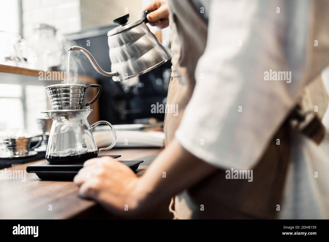 Side view midsection of barista pouring boiling water in coffee filter