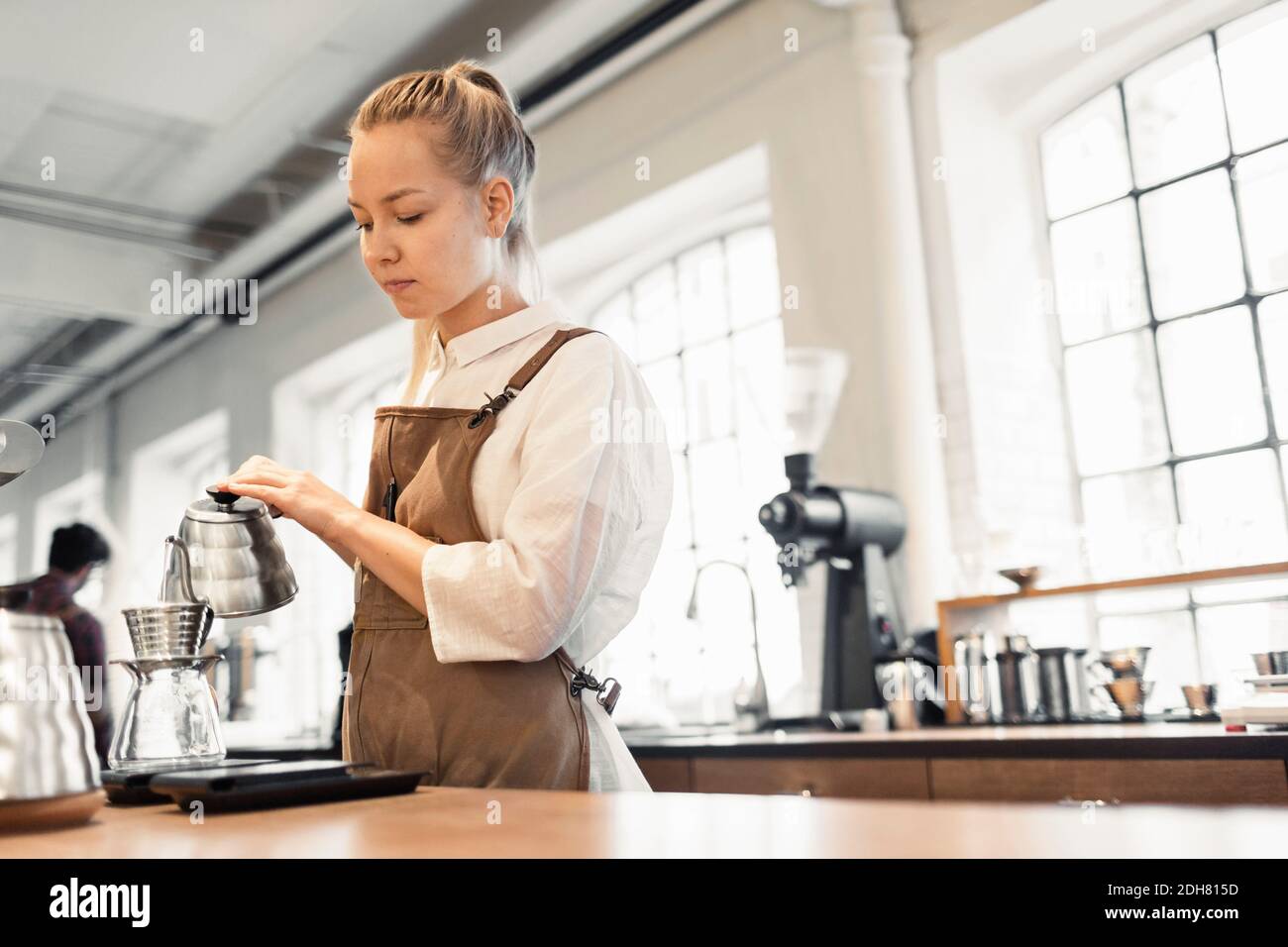 Female barista pouring boiling water in coffee filter at cafe Stock Photo