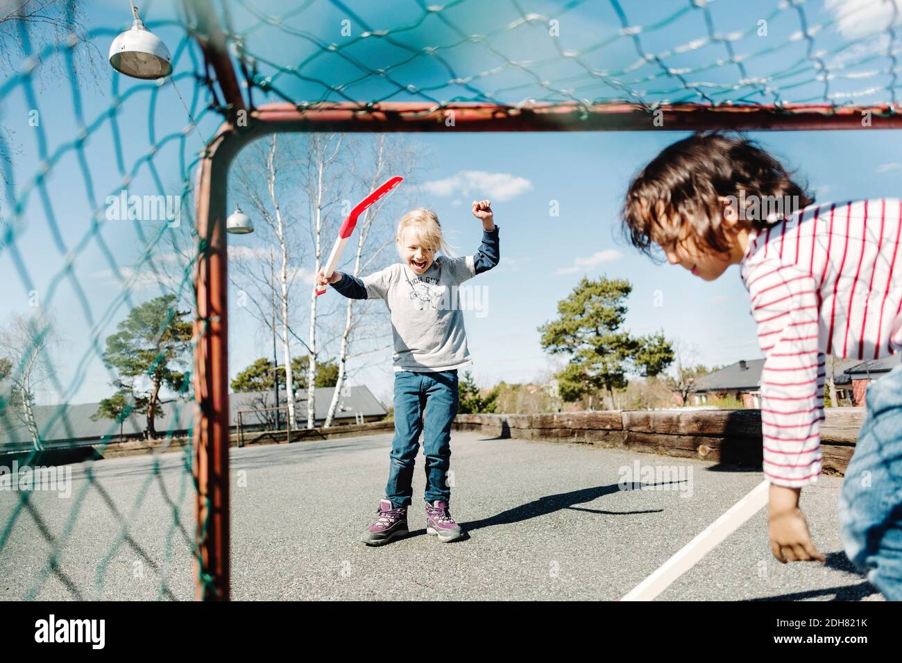 Excited girl gesturing while playing hockey with boy at yard Stock Photo