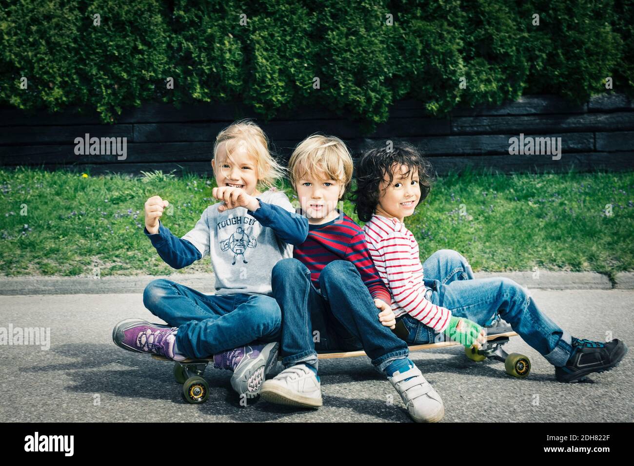 Portrait of happy friends sitting on skateboard against trees Stock Photo