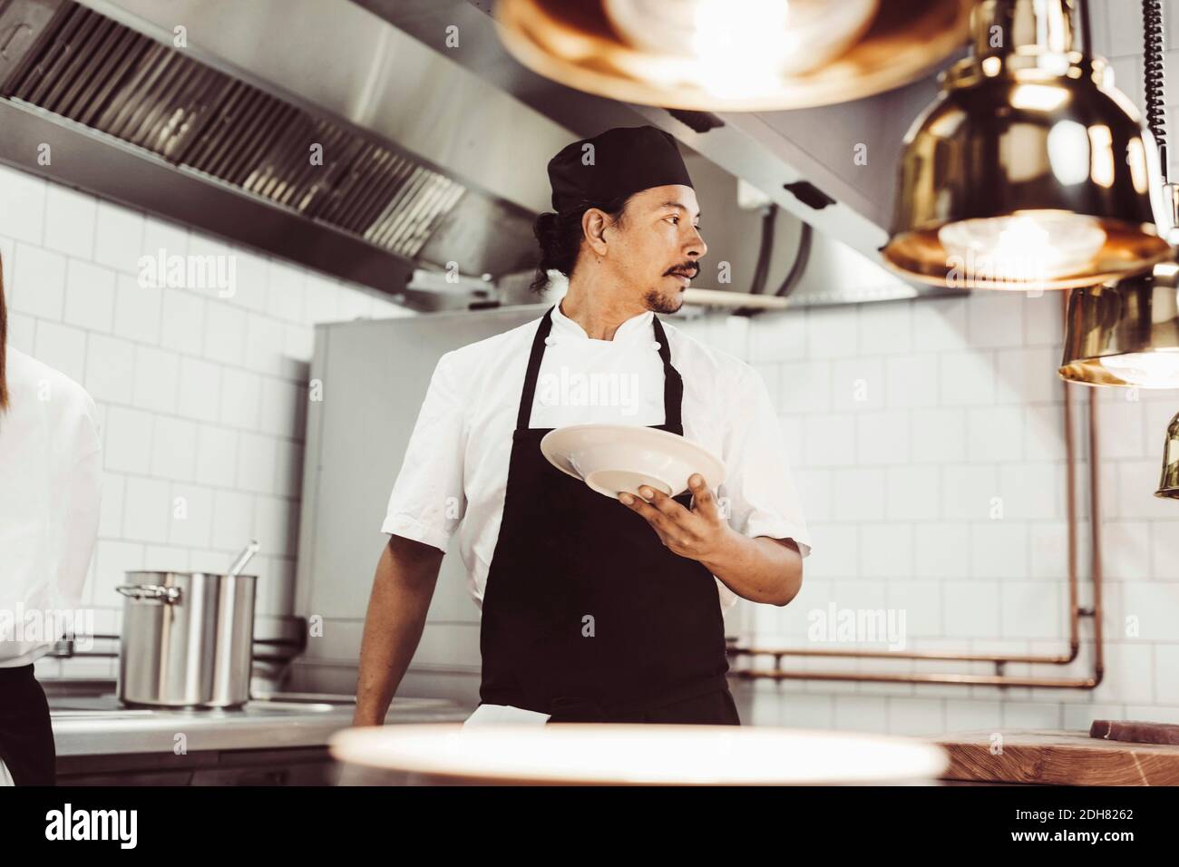 Male chef looking away while holding plate in commercial kitchen Stock Photo