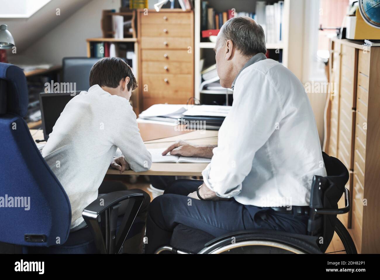 Disabled man assisting son in studying at home Stock Photo