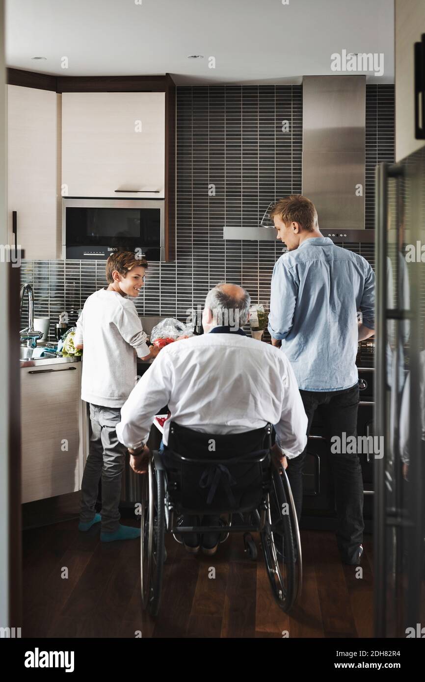 Rear view of disabled father in wheelchair with sons at kitchen Stock