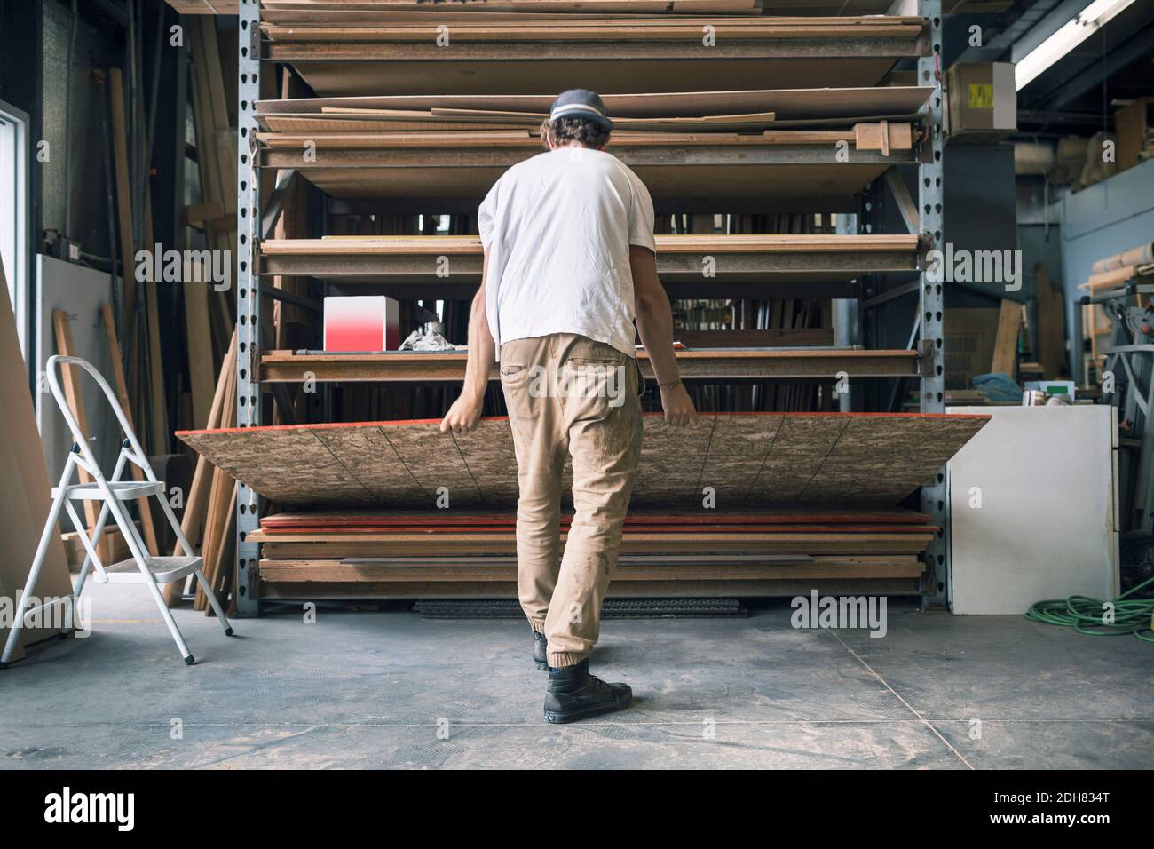 Rear view of man arranging wooden plank in shelf at workshop Stock ...