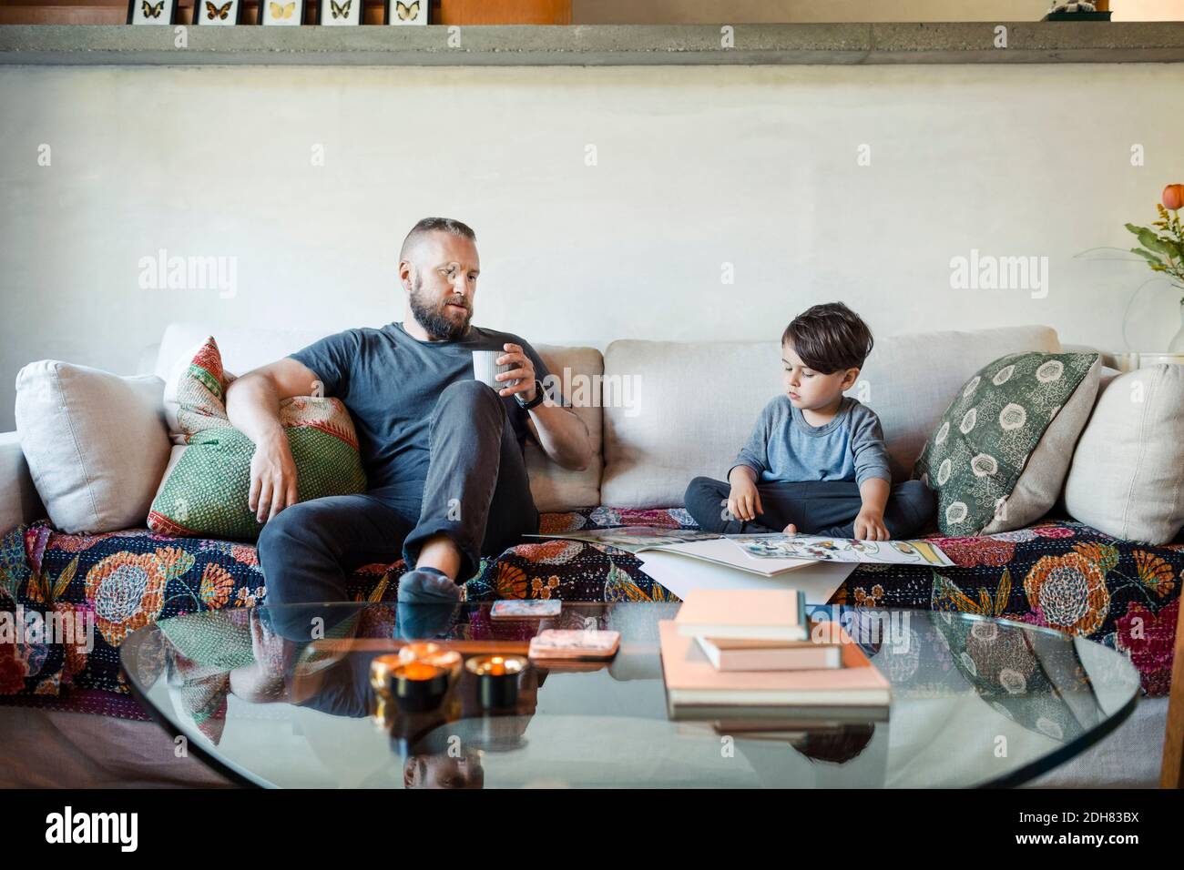 Father holding coffee mug while assisting son in doing homework at home Stock Photo