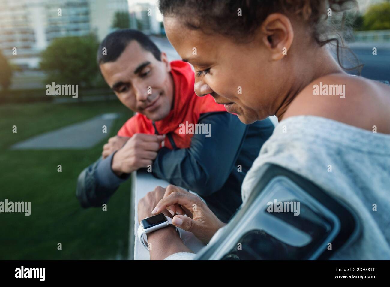 Man looking at friend using smart watch while standing by railing at sidewalk Stock Photo